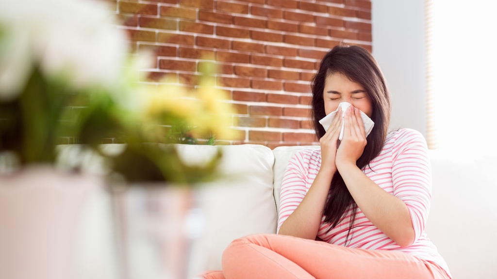 Heuschnupfen: Frau sitzt auf dem Sofa und niest