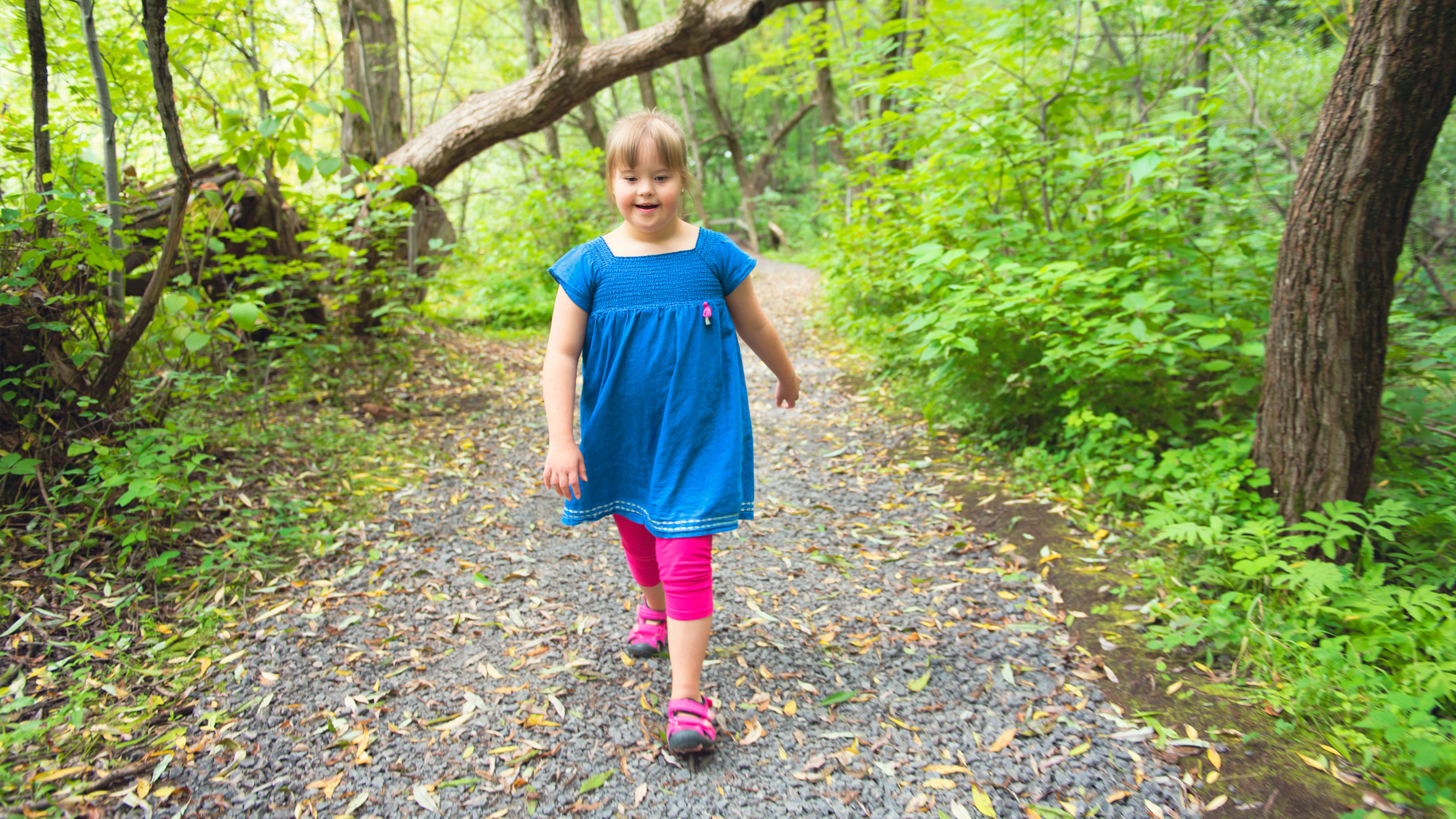 Ein Mädchen mit Trisomie 21 spaziert durch einen Wald.