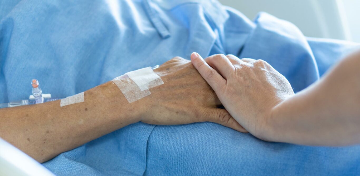 Situation der Palliative Care: Nahaufnahme zweier sich berührenden Hände, eine gehört der Patientin, die andere ist von einer Pflegenden.