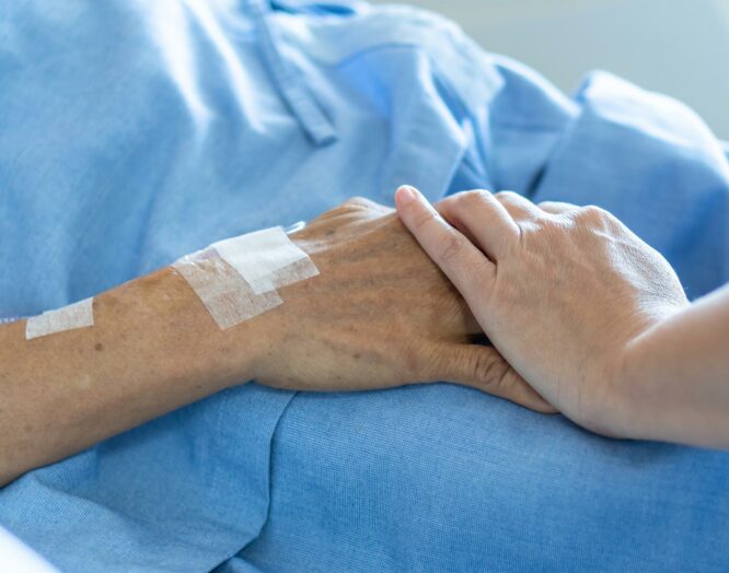 Situation der Palliative Care: Nahaufnahme zweier sich berührenden Hände, eine gehört der Patientin, die andere ist von einer Pflegenden.