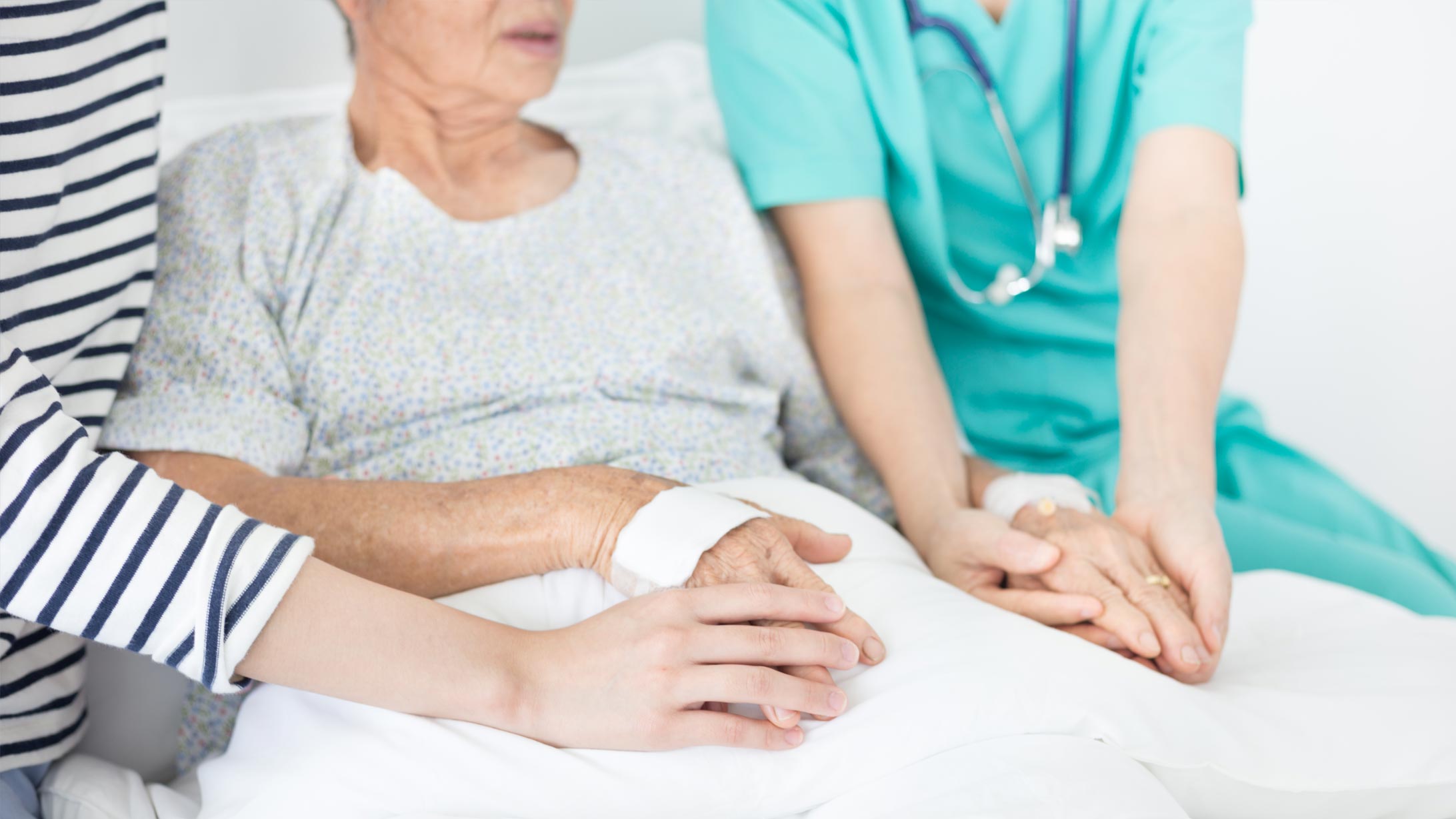 Eine Situation von der Palliative Care: Eine Patientin sitzt im Bett, auf der einen Seite sitzt eine Pflegende, auf der anderen eine Angehörige.