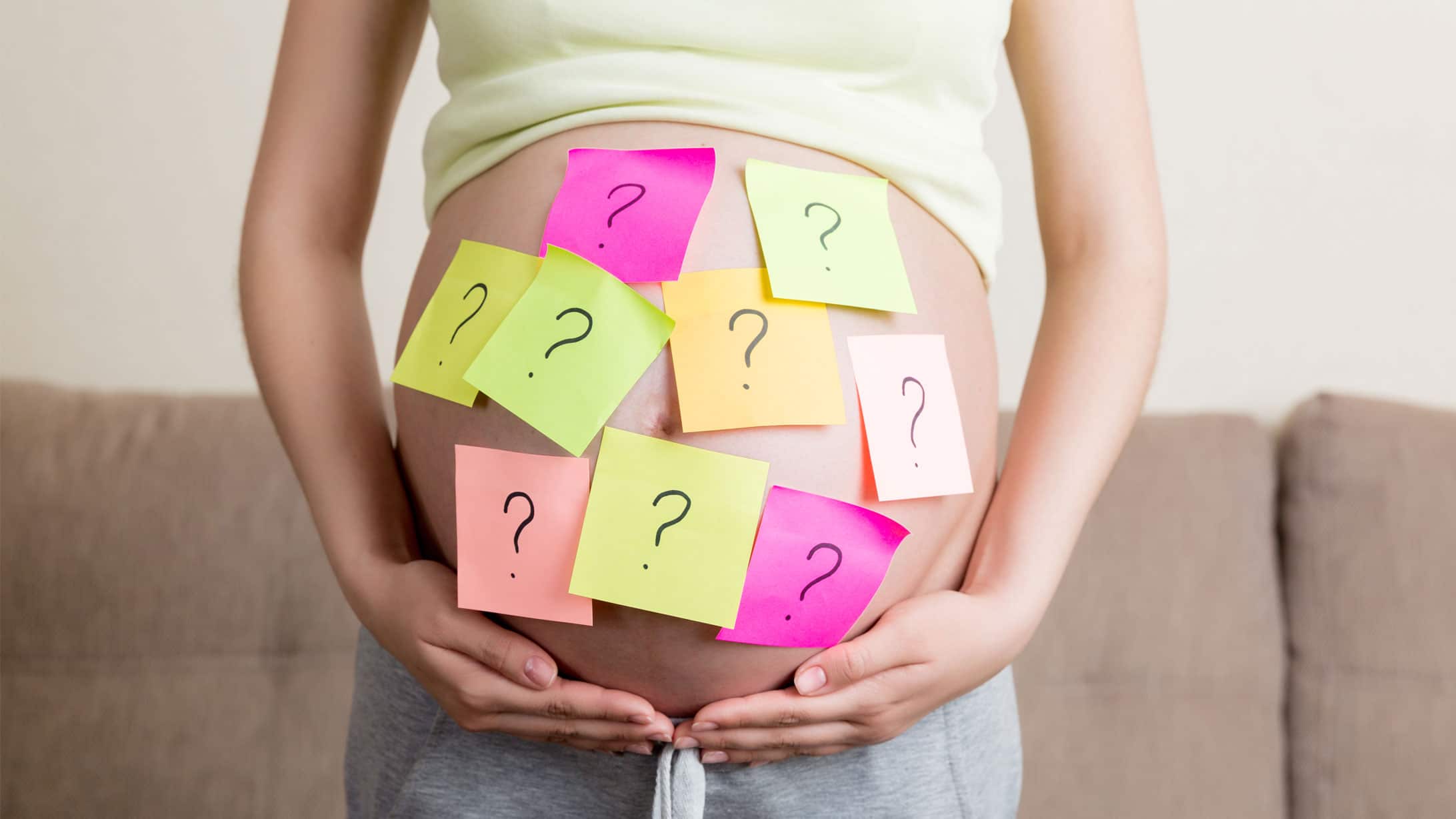 Schwangerschaft: Eine Schwangere hält ihren Bauch. Auf diesem kleben viele farbige Post-Its mit Fragezeichen.