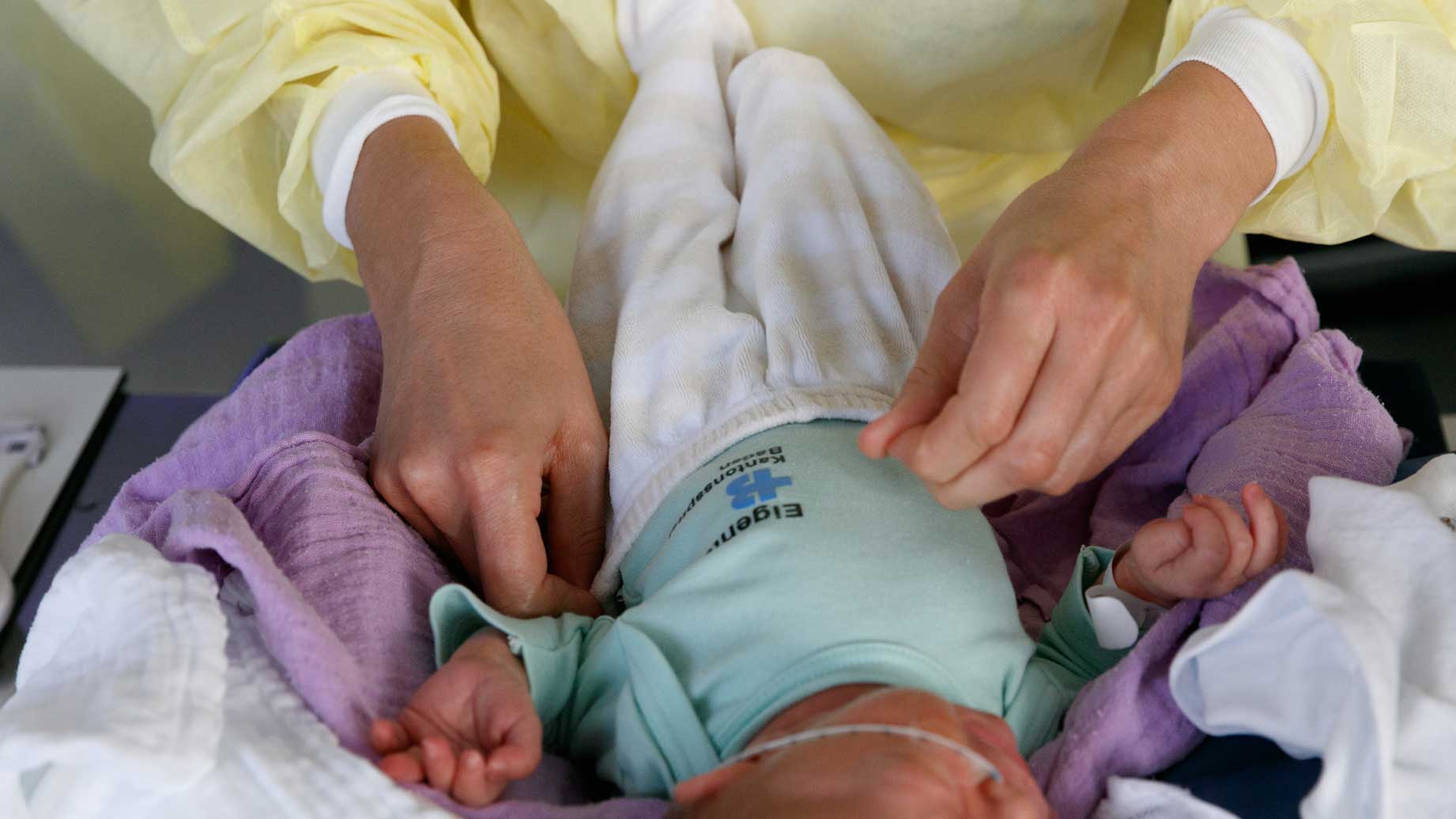 Eine Frau legt einem Neugeborenen eine Strampelhose an.