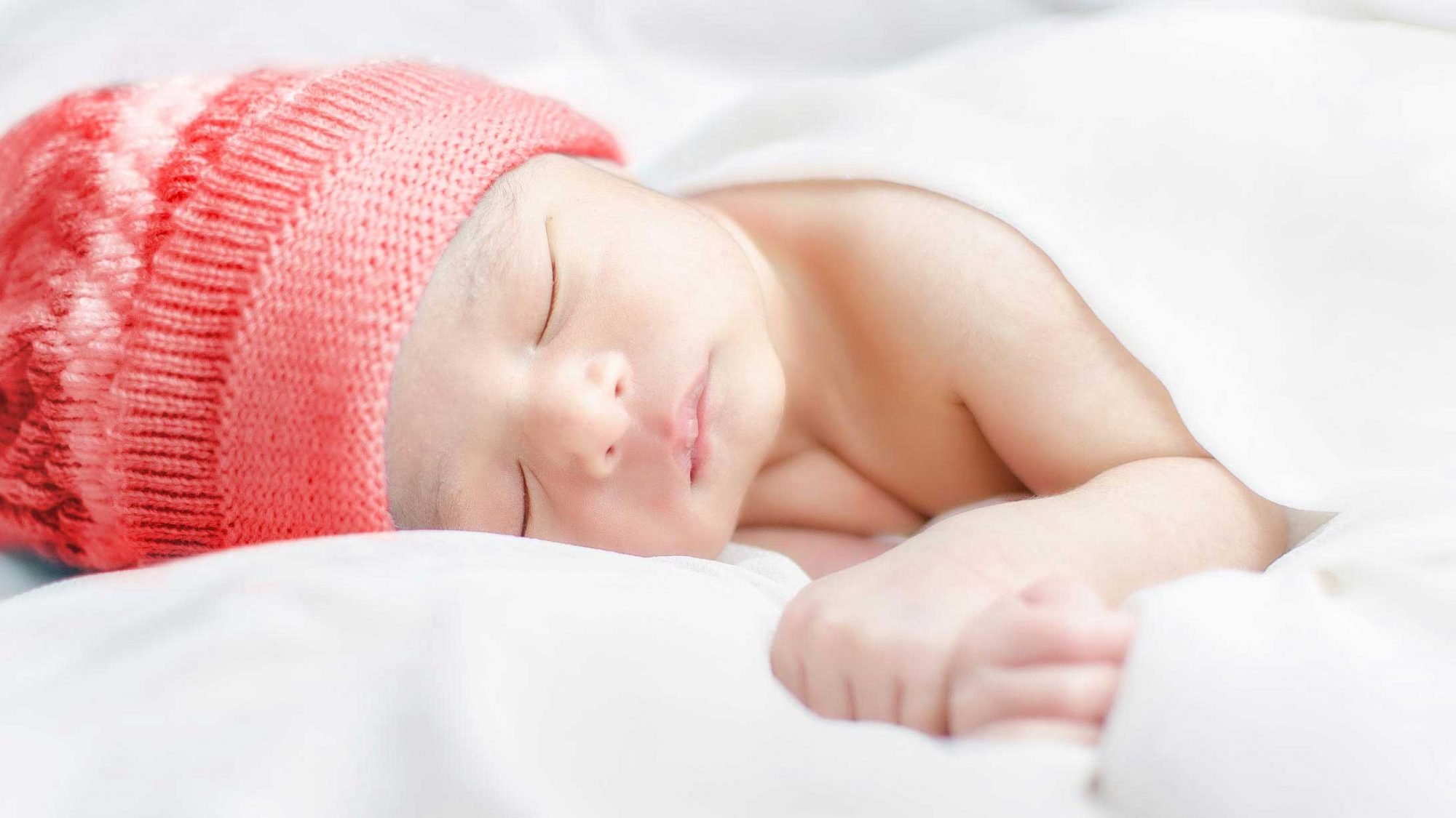 Geburtsrituale: Ein Baby mit einer roten Mütze.