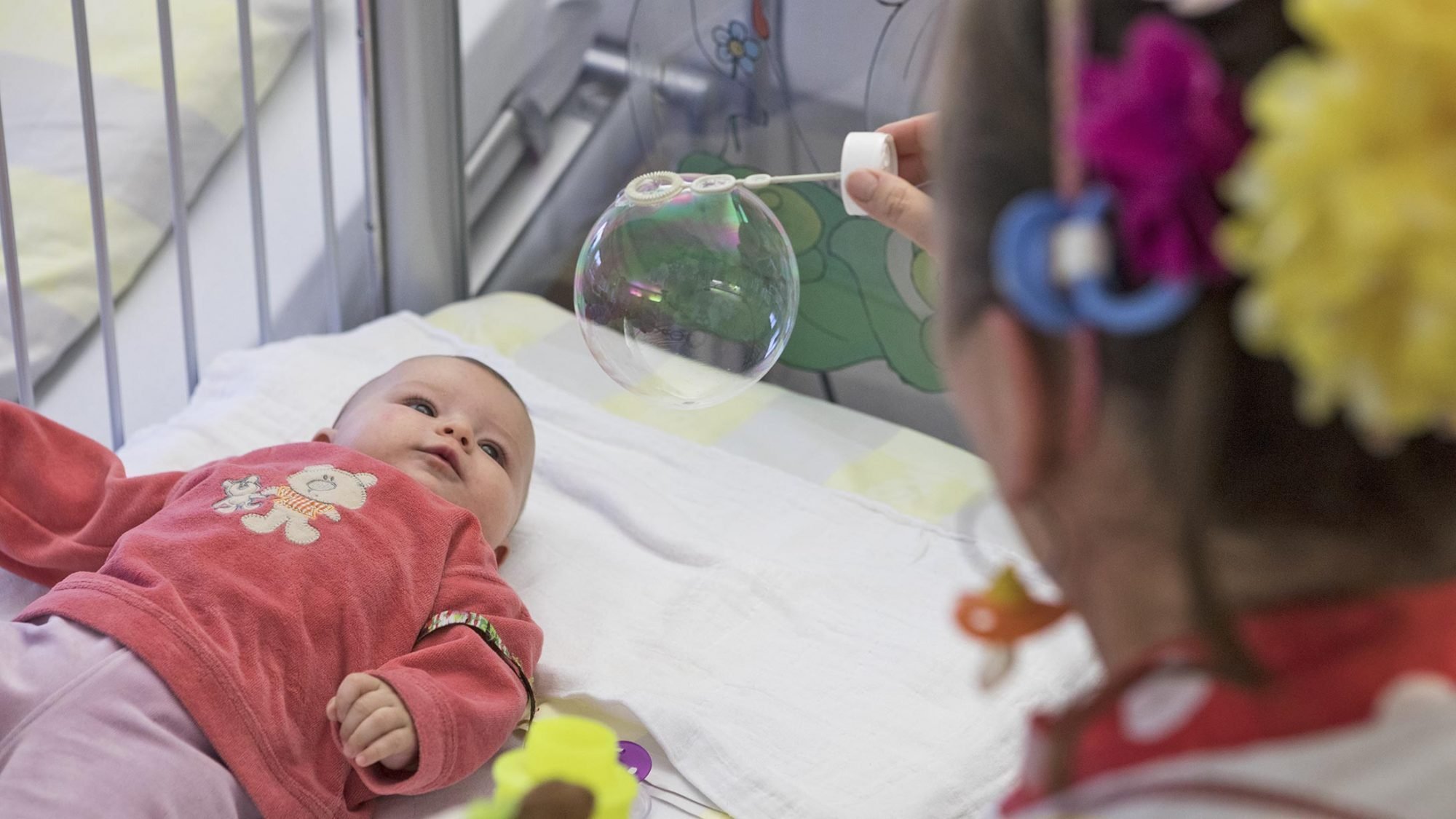Stiftung Theodora: Dr. Floh pustet Seifenblasen über das Bett eines Babys.