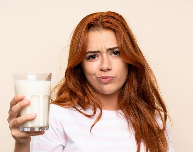 Eine Frau hält ein Glas Milch in der Hand. Sie schaut fragend – leidet sie vielleicht an Laktoseintoleranz?
