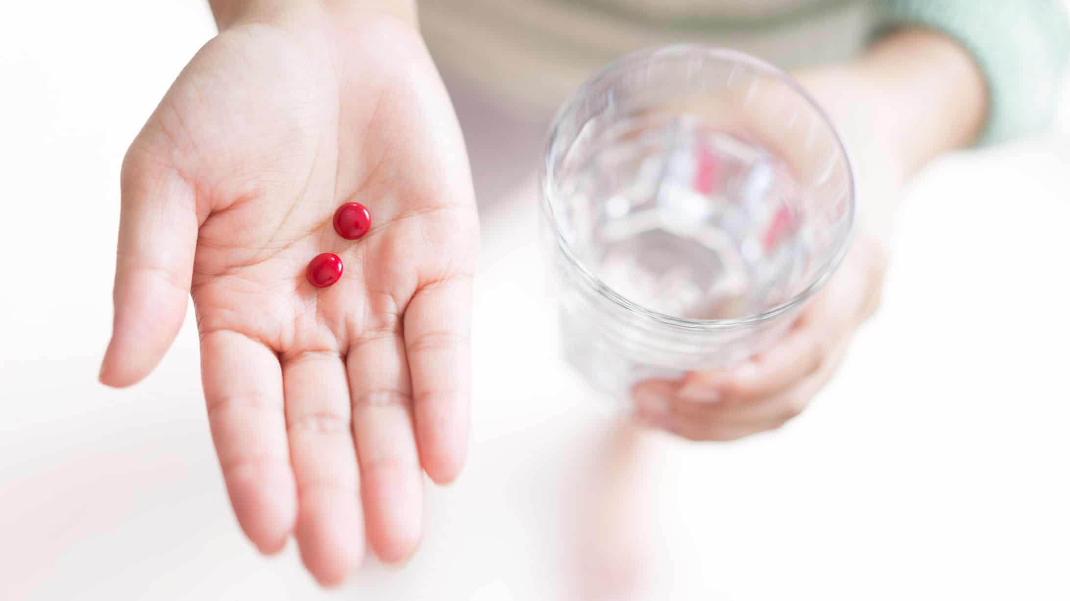 zwei rote Pillen in der Hand einer Frau. Glas Wasser in der anderen Hand