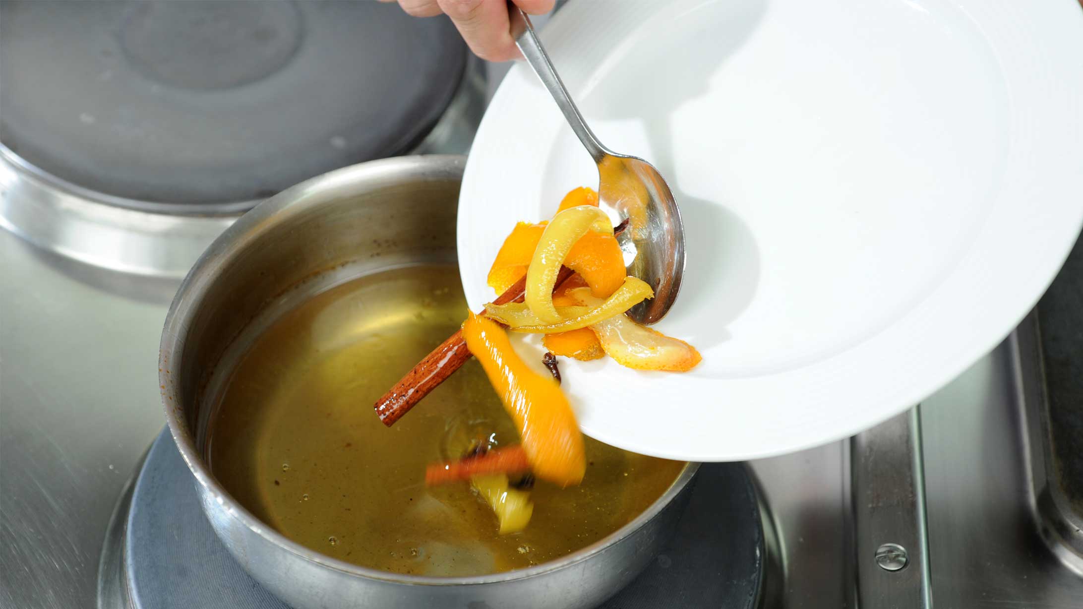 Orangenschalen und Zimtstangen werden in einen Topf mit Öl gegeben.