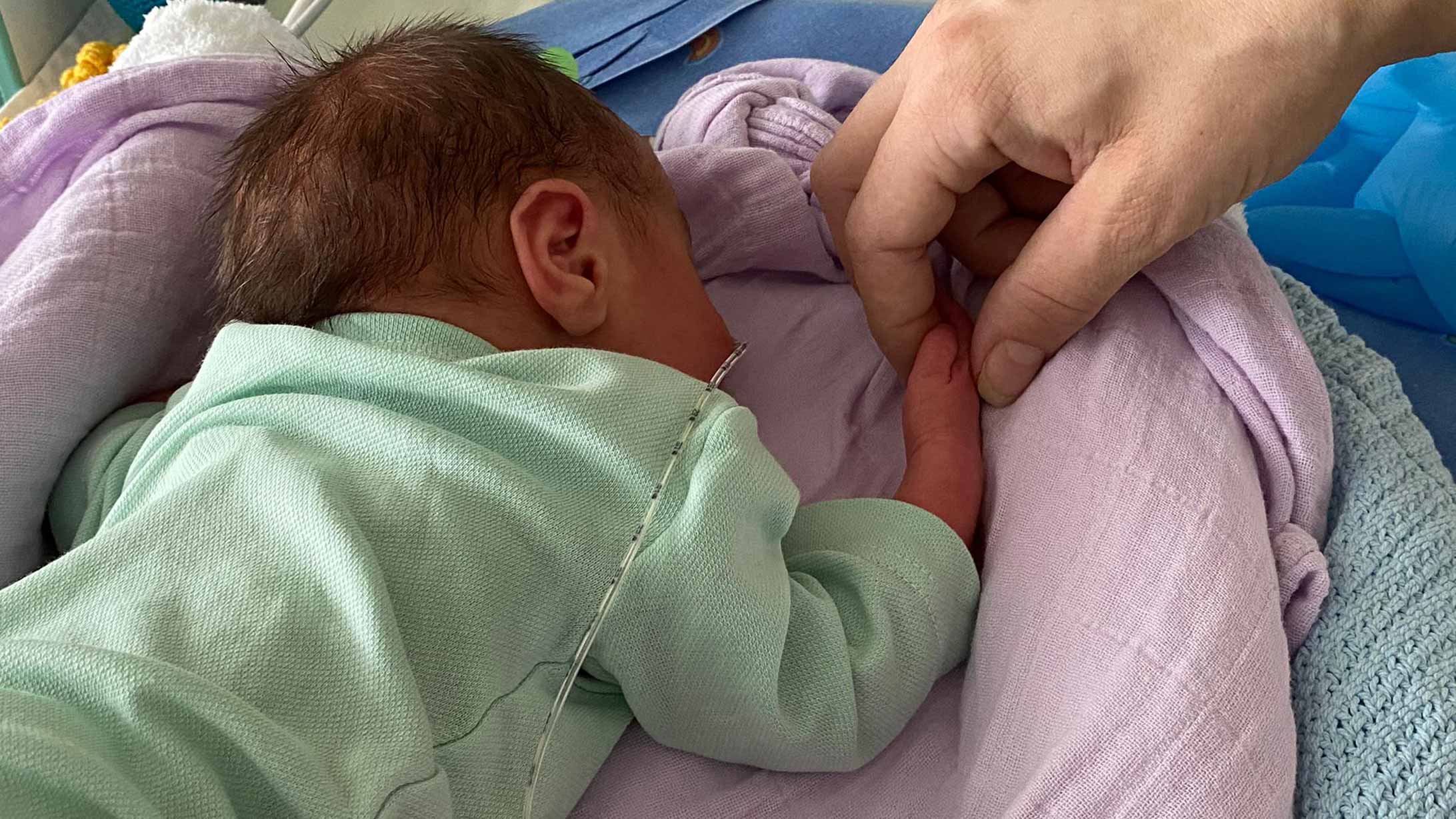 Ein Neugeborenes liegt im Bett und hält eine Hand