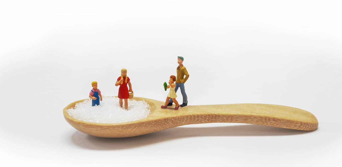 Diabetes Typ 1: Spielfiguren stehen auf einem mit Zucker gefüllten Holzlöffel