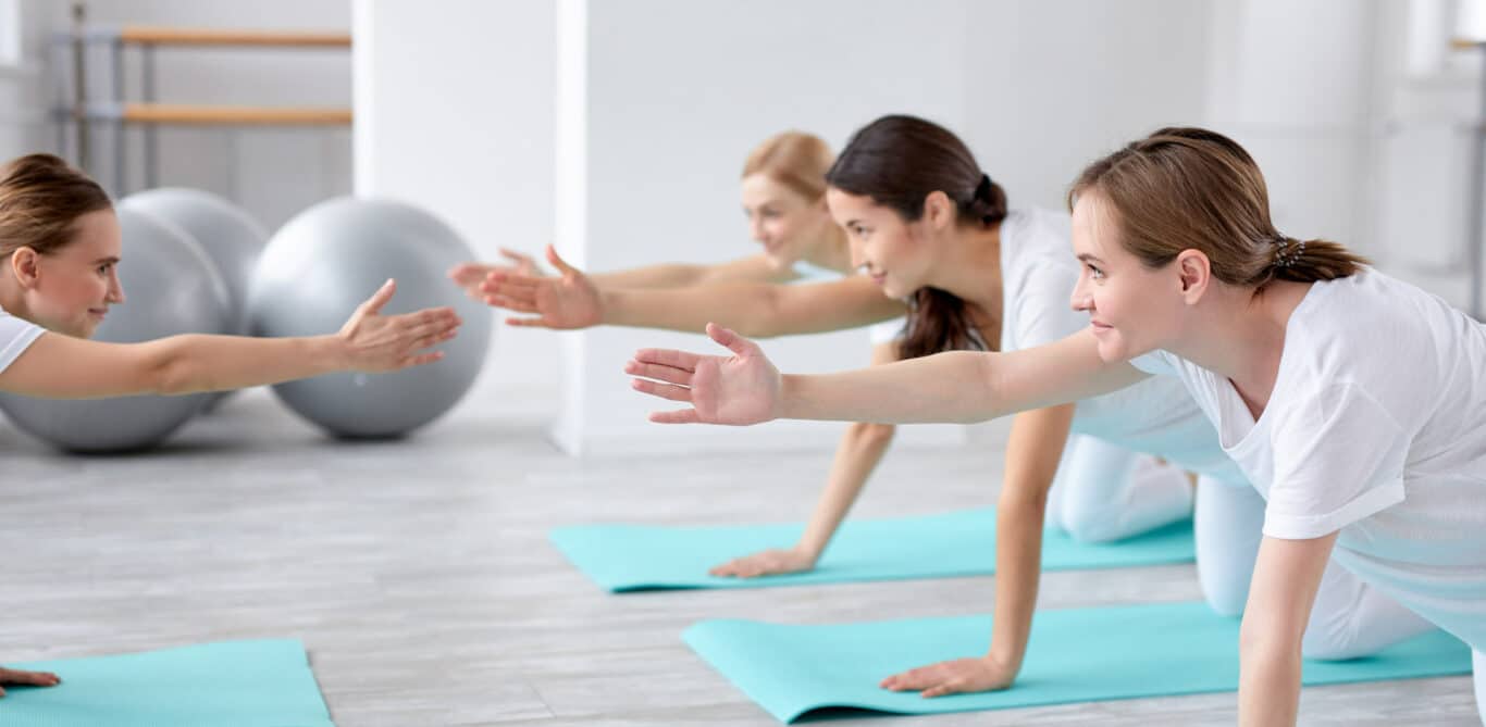 Eine Gruppe junger Frauen macht in einem Fitnessraum Übungen auf Yogamatten