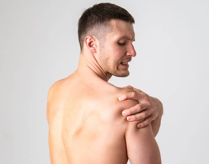 Ein Mann fasst sich mit schmerzverzerrtem Gesicht an die Schulter. Symbolbild für Impingement an der Schulter.