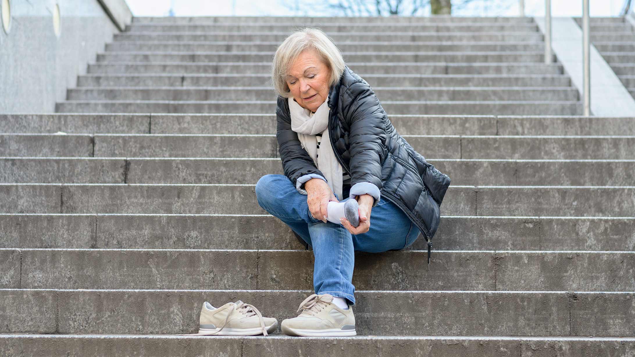 Eine Frau sitzt auf einer Treppe und hält sich Fuss und Knöchel